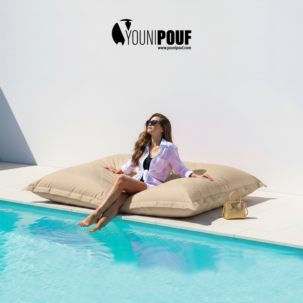 Moment de relaxation au bord de la piscine sur un pouf XXL beige YOUNIPOUF confortable et design.